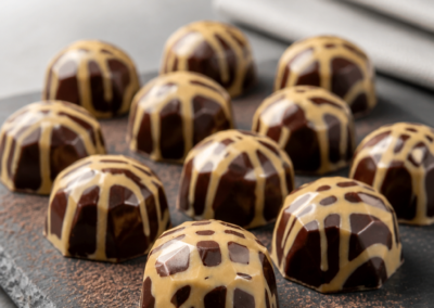 Glossy dark chocolate domes striped with caramel-colored stripes on a slate plate